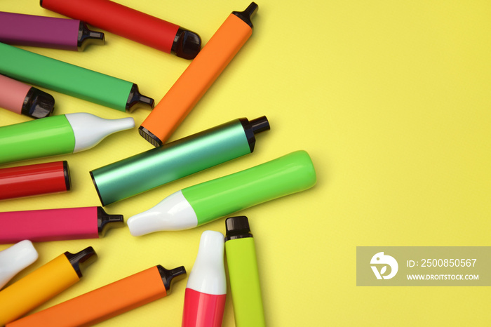 Set of multicolor disposable electronic cigarettes on a bright yellow background.