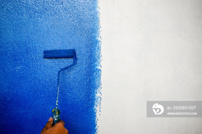 Male hand painting wall in blue with paint roller