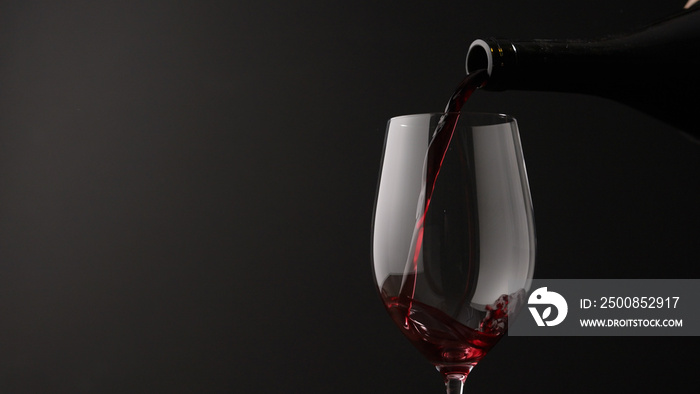 pour red wine into wineglass on black background