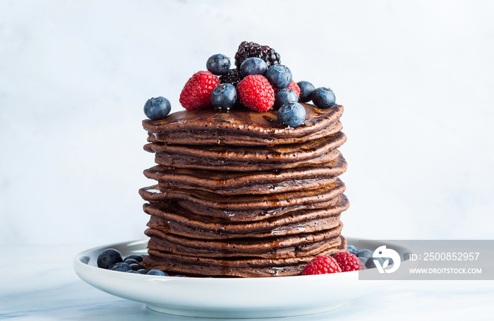 Flowing maple syrup on a pile of chocolate pancake with fresh berries. morning healthy breakfast