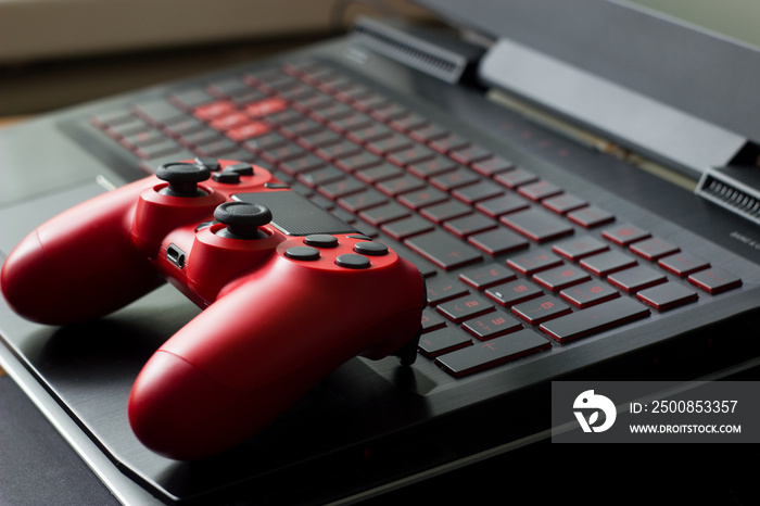 Side view on black gaming laptop computer keyboard and modern red gamepad. Gaming concept