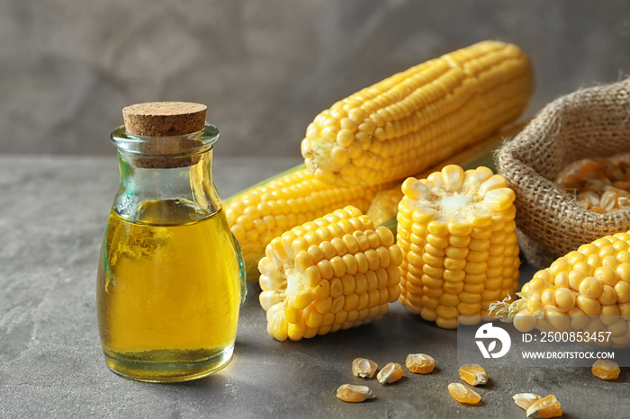 Glass jar with corn oil on grey background