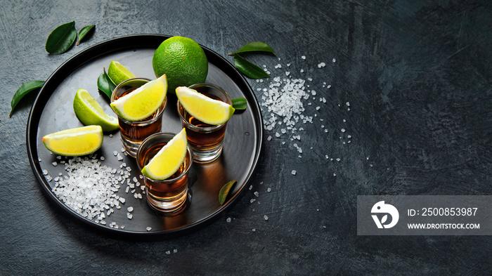 Tequila shots with lime and salt on gray background.