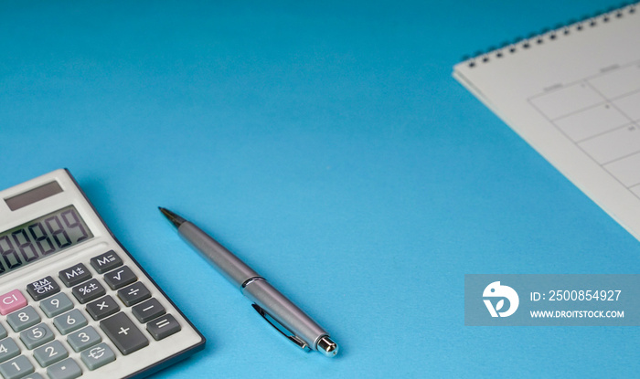 Calculator, pen and table calendar on blue background. Top view of office desk.