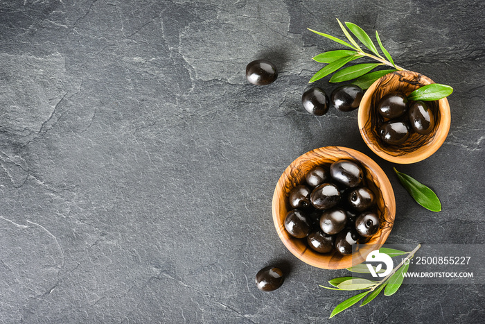 Fresh green and black original olives on black background. Olive concept on wooden cut board at dark stone table.