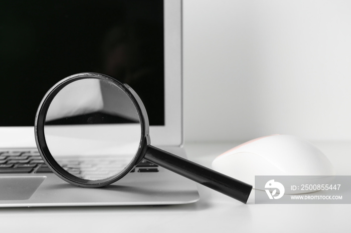 Magnifier, laptop and computer mouse on white table, closeup. Internet search concept