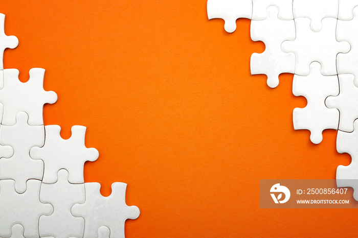 Jigsaw puzzle pieces and business concept with a border made of puzzle pieces on colorful bright orange background with copy space