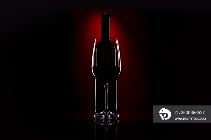 Glass and bottle of red wine on a dark red background