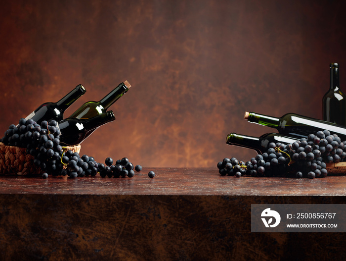 Juicy blue grapes and bottles of red wine on a brown background.