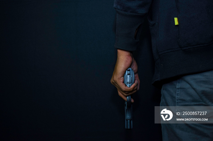 asian man holds a gun. Gun in his hand from the back isolated on black background.