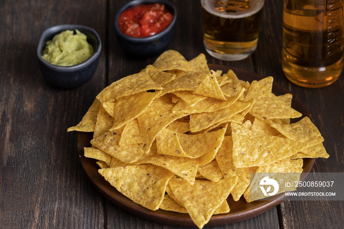 Nachos with guacamole, red chilli sauce and beer  on wooden table The most famous Mexican snack background.