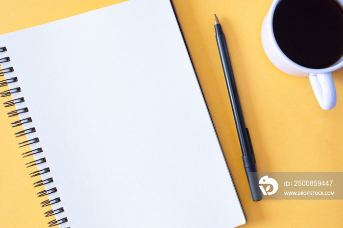 Directly above view of notepad, pen and coffee cup on yellow background.