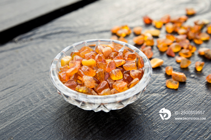 Cute little bowl cup full of small Baltic amber chips on dark brown wooden background. The Baltic region is home to the largest known deposit of amber, called Baltic amber or succinite.