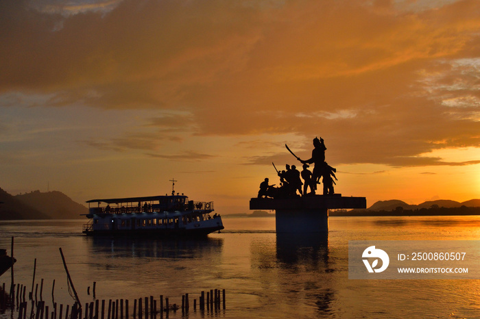 Silhouette of Lachit Borphukan statue during sunset with a ship passing in background in river brahmaputra.