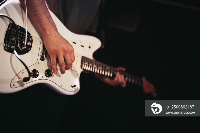 Detail of man playing white electric guitar during a indie rock concert.