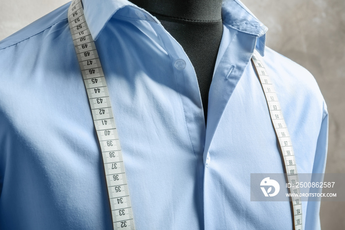 Shirt with measuring tape on tailor mannequin against light background