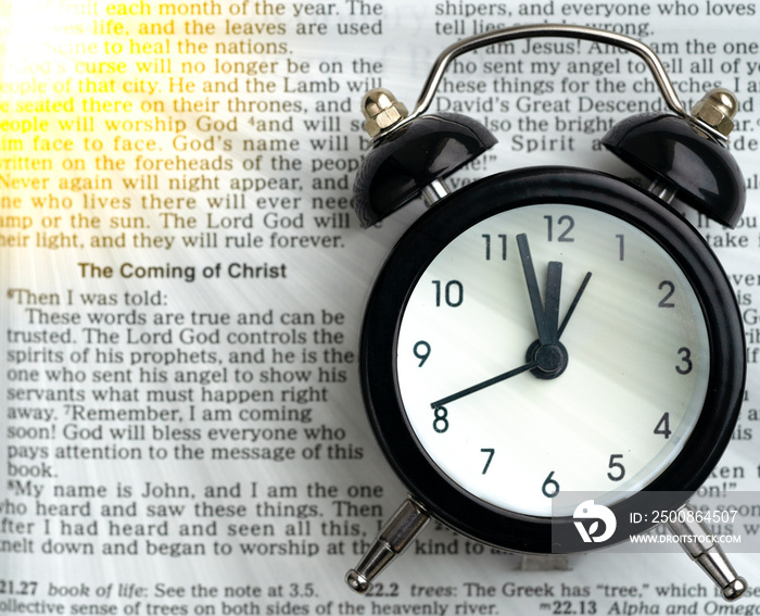 black alarm clock on the open Bible on a white surface