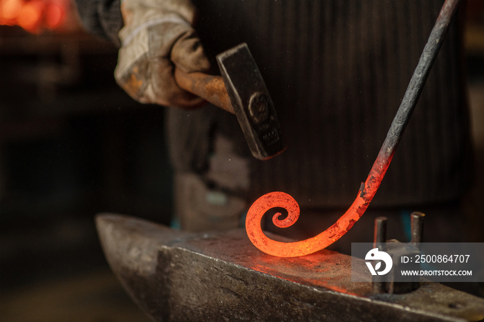 The blacksmith hits the red-hot workpiece in the forge with a hammer and glowing sparks fly in all directions