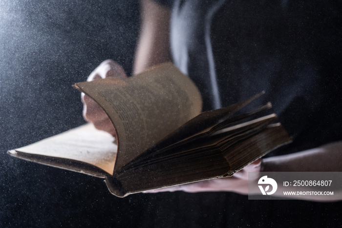 Hands hold Vintage open Book Glows on black background. Concept of mystery, riddle and secret