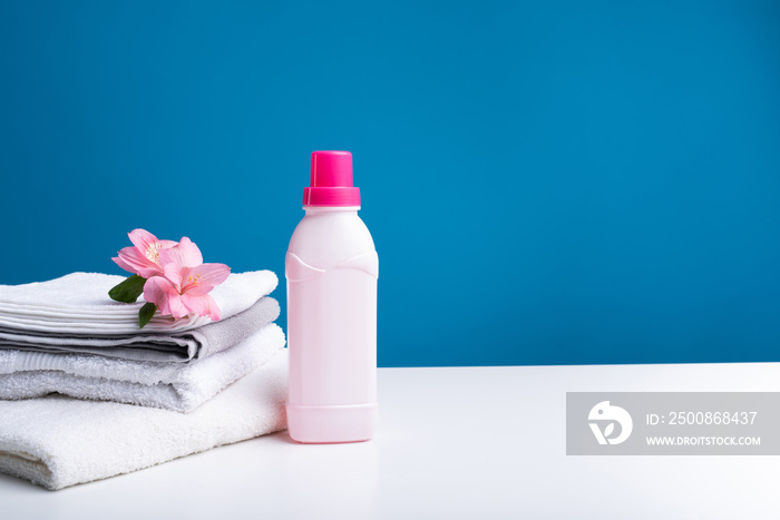 Close up of washed towels folded in heap with flower on top. Can of abstergent standing beside. This softener will bring you real natural freshness and gentleness. Copy space in right side