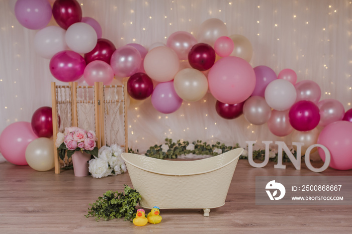 First birthday smashcake photo session with pink balloons and flowers and a vintage bathtub in a photo studio