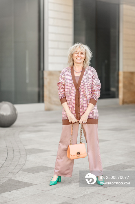 Attractive adult blonde of European appearance in a pantsuit with a handbag in her hands on the streets of the city