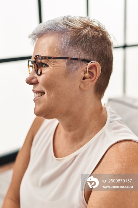 Middle age woman using hearing aid sitting on sofa at home