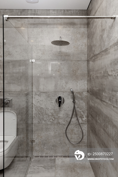 Part of the bathroom in gray tones, tiles on the walls, shower with steel faucets.