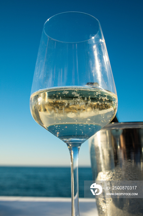 Expensive dinner at sunset on a beach restaurant with amazing sea view. Close up of a glass of white sparkling whine with ice bucket in the background.