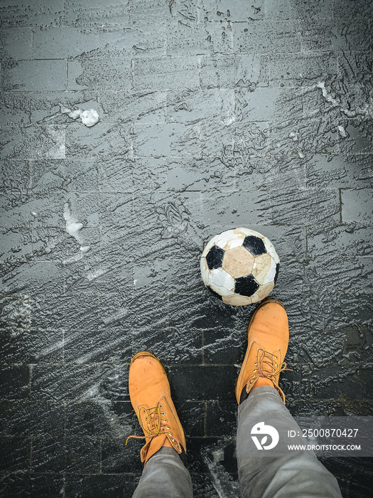 First person point of view down on the man feet wearing yellow boots.  Paving tile covered with slush in winter. Playing football during snow