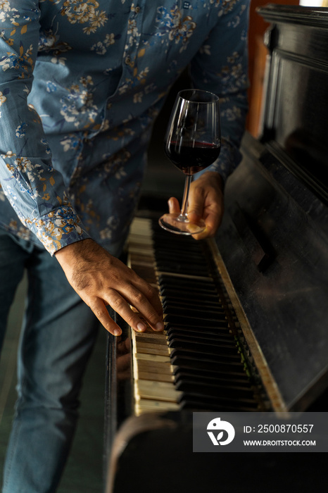 A glass of wine at a man’s hand in front of a vintage piano