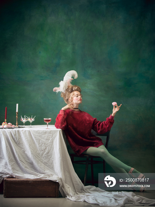Marshmallow sweet. Young woman as Marie Antoinette isolated on dark green background. Retro style, comparison of eras concept. Beautiful female model like classic historical character, old-fashioned.