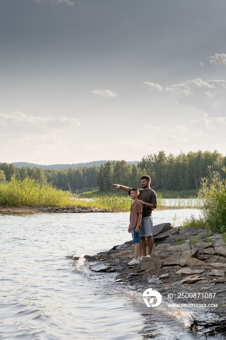 Father and teenage son standing in front of waterside during summer rest in the country