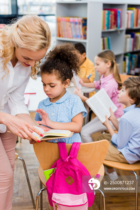 selective focus of woman standing near cute african american kid with book