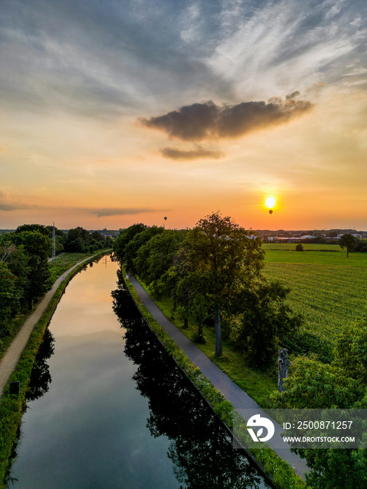 Colorful and dramatic sunset over the canal Dessel Schoten aerial photo shot by a drone in Rijkevorsel, kempen, Belgium, showing the waterway in the natural green agricultural landscape. High quality