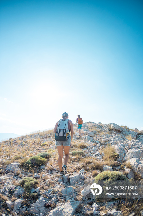 two girls with backpacks walk along a mountain path.