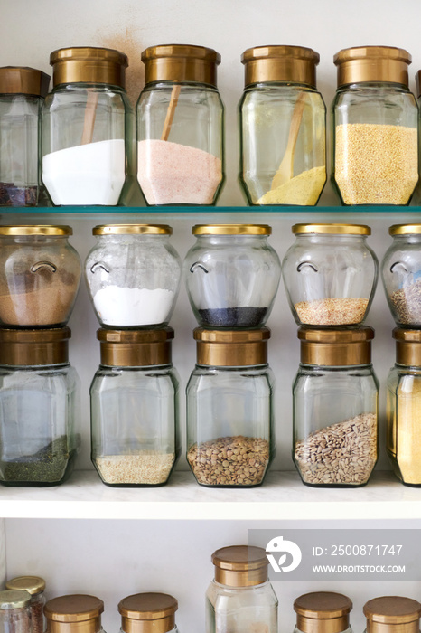 Kitchen supplies, many ingredients and spices in glass jars placed orderly on a kitchen shelf