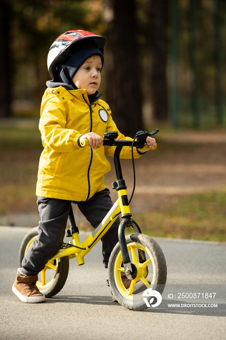 Little boy in protective helmet riding balance bicycle along asphalt road