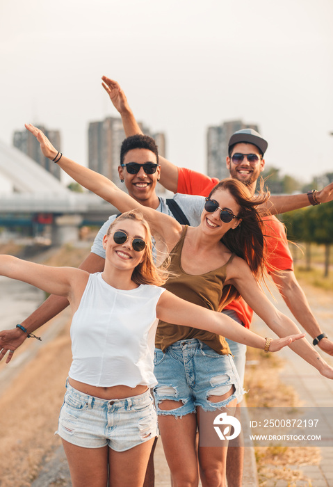 Portrait of group of young friends standing by the river in the city with arms outstretched and looking at camera.