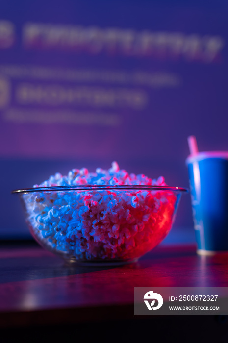 Popcorn in a glass bowl and a soda drink in a glass. Close-up. Carefree viewing of television programs, favorite films. Holiday symbols. Neon lighting. Close-up.