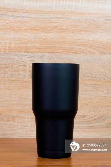 Black colour stainless steel tumbler or cold storage cup on wood background.