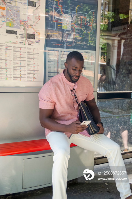 Man with briefcase and smart phone sitting at bus stop