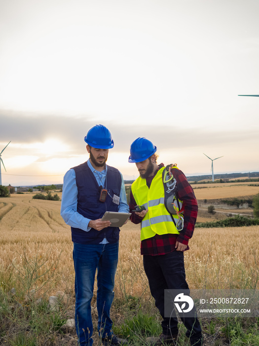 Two male workers looking at data on a tablet in a windmill field. Renewable energies, engineers