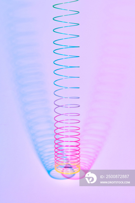 Vertical rainbow plastic slinky toy with two color shadows.