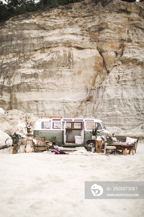 Wedding decor in boho rustic style. Green hippie bus, decorated sofa, armchair, carpets, pillows, table with candles, succulents, plant decoration on the background of canyon landscape