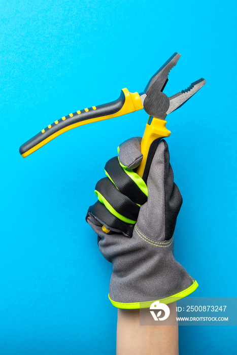 Pliers. Yellow and black pliers in the hand of an electrician on a blue monochrome background. Repair and installation tool. Banner for the design and printing of construction topics.