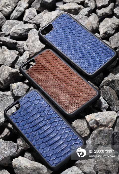 Three exclusive brown and blue snake leather case for smartphone.Luxury case. On stone background