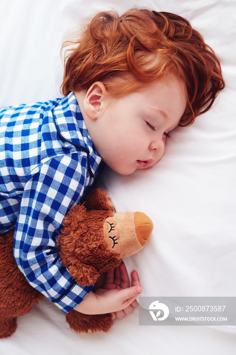 adorable redhead toddler baby sleeping with plush toy in flannel pajamas