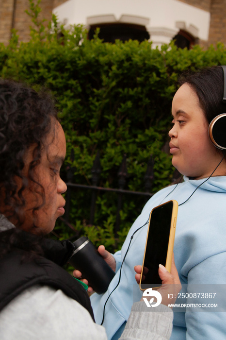 Two curvy women with Down Syndrome listening to music in an urban environment