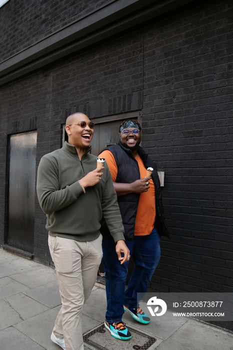 Two smiling men in front of black wall enjoying ice cream